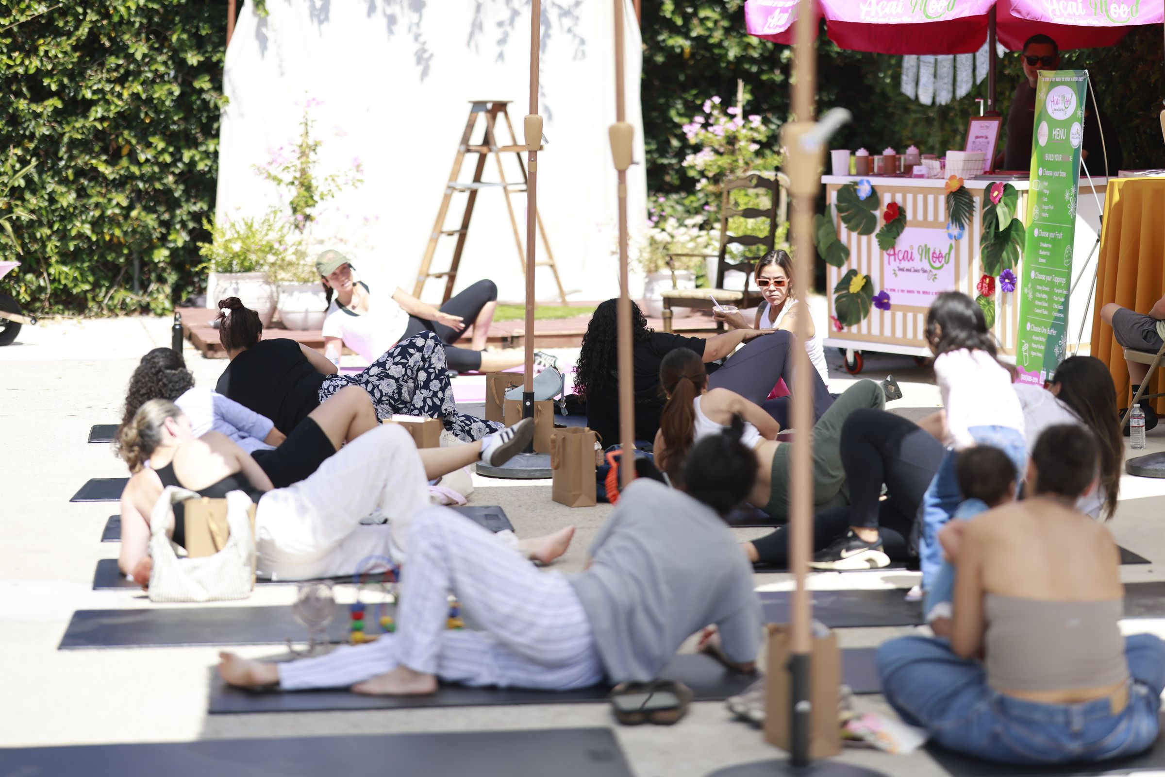 Mothers on mats in a movement class outdoors at a Salud Wellness gathering, with babies and strollers beside them.