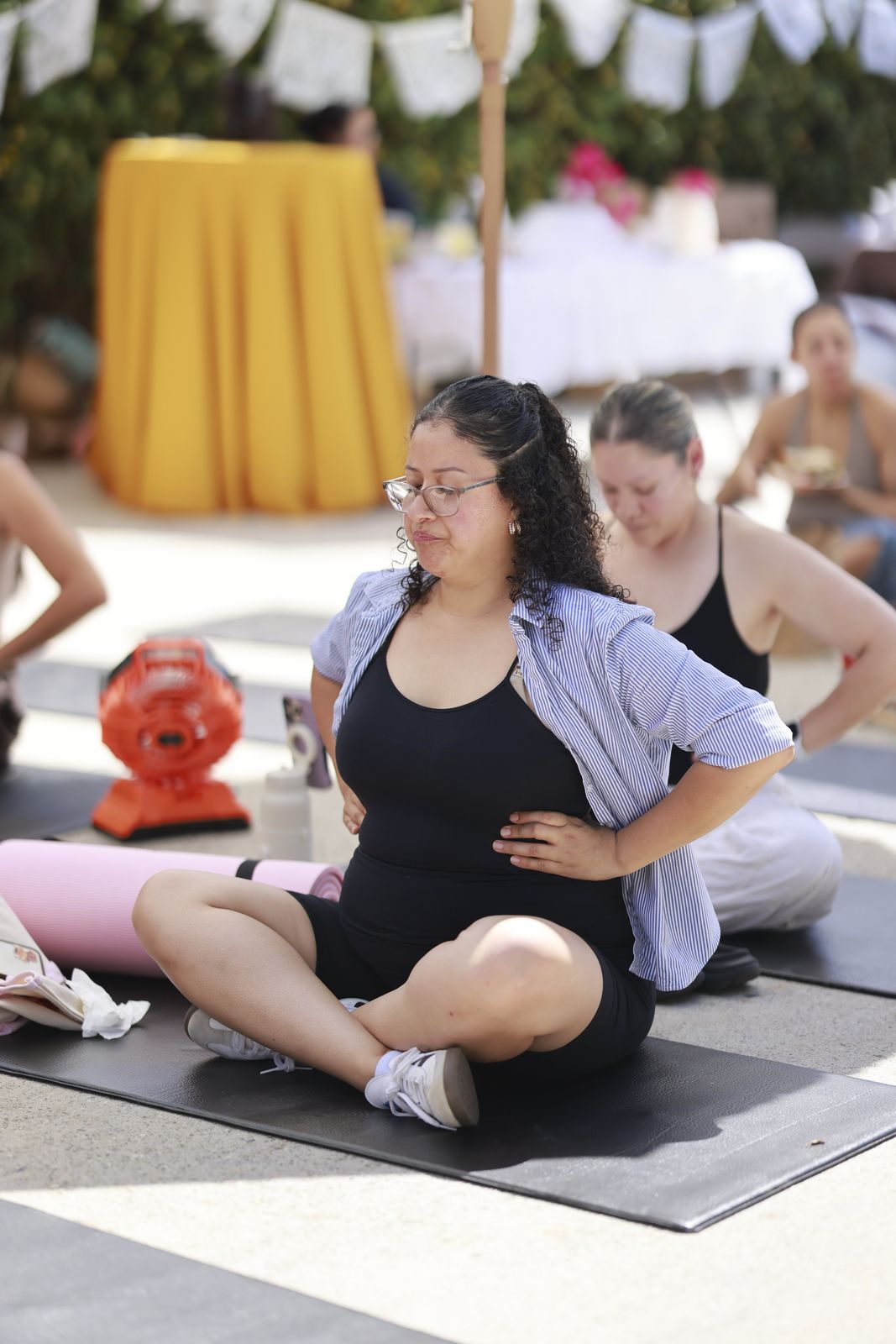 A mother seated cross-legged on her mat with her hands at her waist, following the session.
