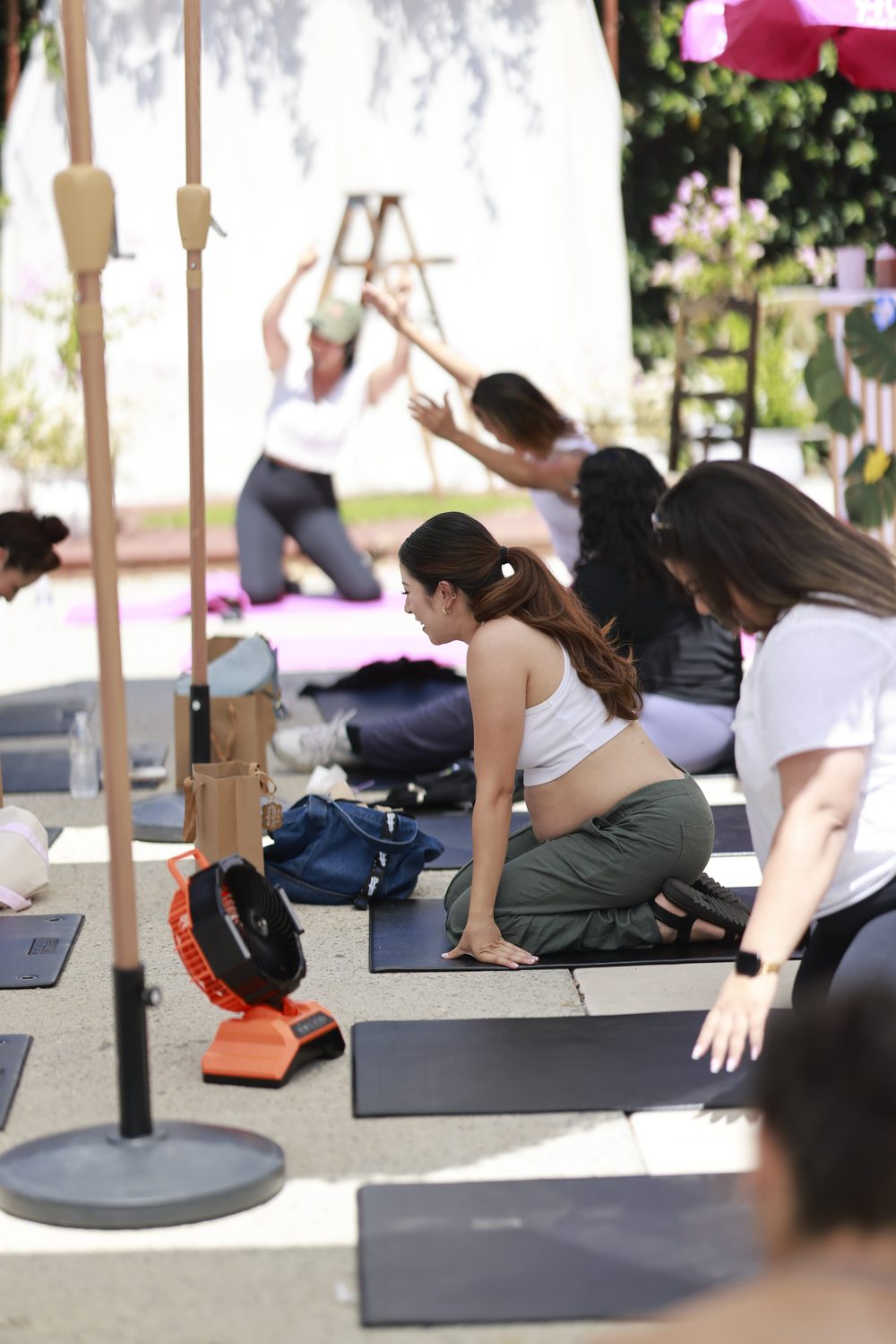 An expecting mother smiling on her mat as the group stretches under the umbrellas.