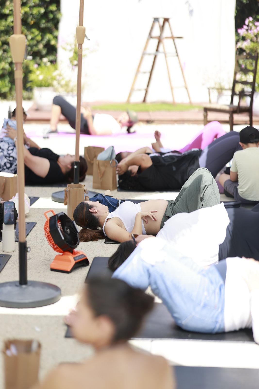 Mothers resting on their backs on mats between umbrellas, one expecting mother with a hand on her belly.