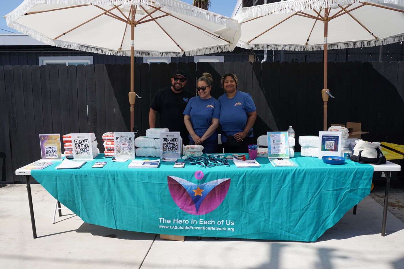 Three staff members from the LA County Department of Mental Health at a resource table stocked with diapers and wipes for families, at Mothering the Mother.